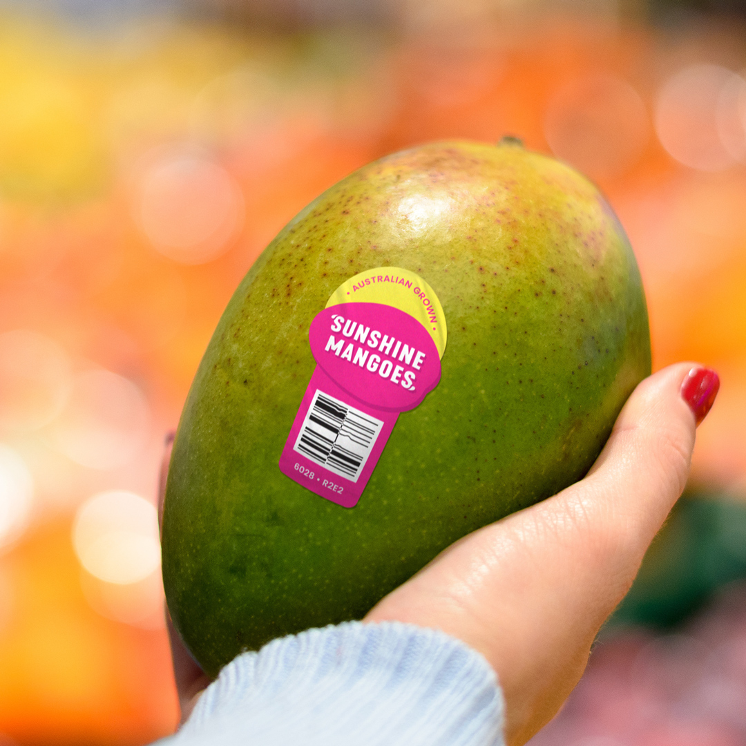 Woman holding a mango with a Sunshine Mangoes' fruit sticker